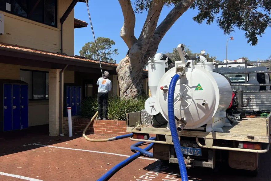 Michael using gutter vacuum equipment beside a building.