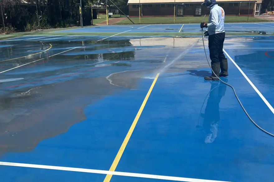 Michael pressure cleaning a blue outdoor sports court.