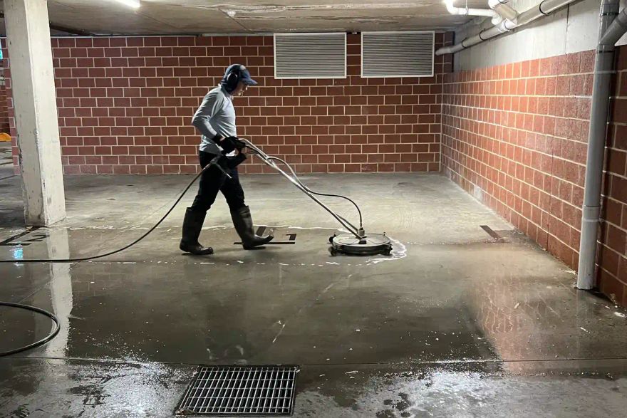 Michael pressure cleaning a concrete garage floor at a strata complex.