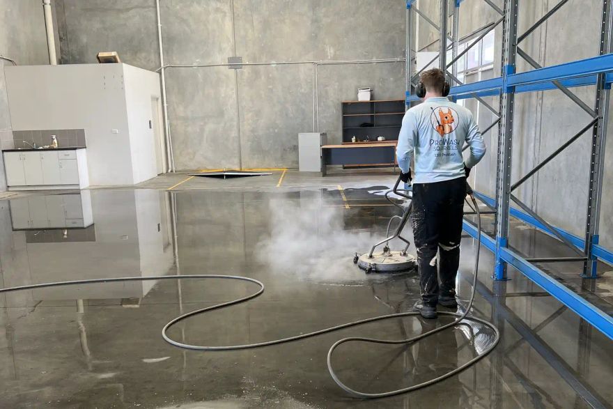 Michael pressure cleaning a warehouse floor beside storage racking.